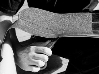 A skateboarder cutting his new grip tape with his Ellis EDC multitool pocket knife.
