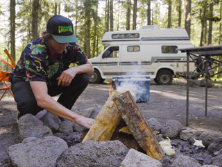 A man starting a camp fire with his RV in the background. 