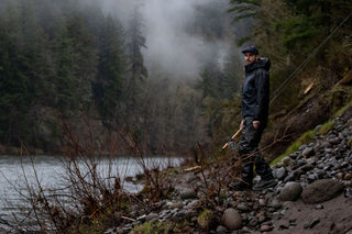 A man walking to the bank of a river to fish. 