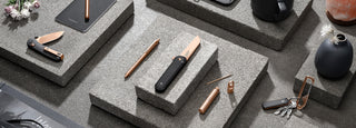The Rose Gold Collection of EDC pocket knives, pens, and keychain carabiners displayed on blocks.