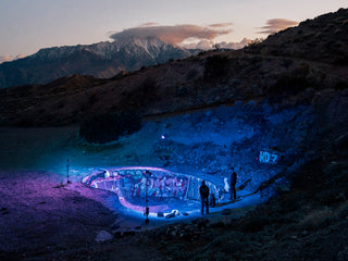 A group of skaters hanging out at the Nude Bowl with snow capped mountains in the background.