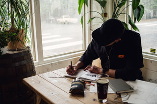 A man sketching in a notebook at a cafe with his Bolen titanium EDC twist pen.