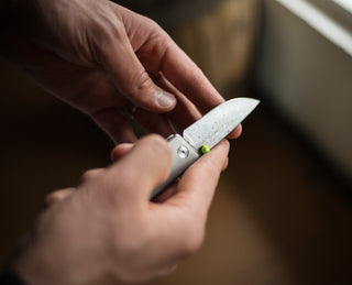 The Chapter 2 EDC titanium pocket knife with a Damasteel blade in hand.