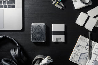 Silver wallet on a black box with keys and books in the background.