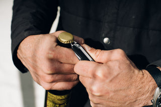 A man using the pry bar on the Ellis ultra slim pocket knife to open a beer.