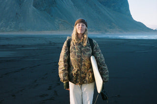 Snowboarder, surfer, and photographer Caley Vanular posing on a Icelandic beach with her surfboard under her arm.