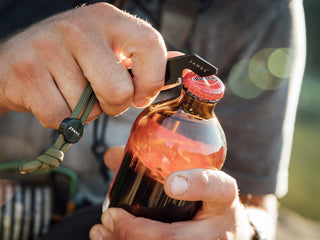 A man opening a bottle of beer with his Halifax EDC keychain multitool.