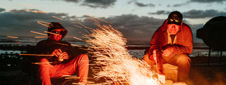 Two guys having a beer next to the bonfire on the beach in Baja.