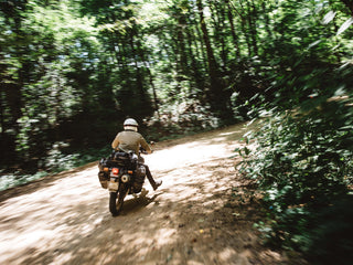 A motorcyclist riding on a dirt road through an Arkansas forest.