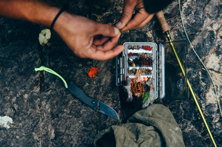 A man tying fishing lures with his Carter EDC slide lock folding pocket knife next to the tackle box.